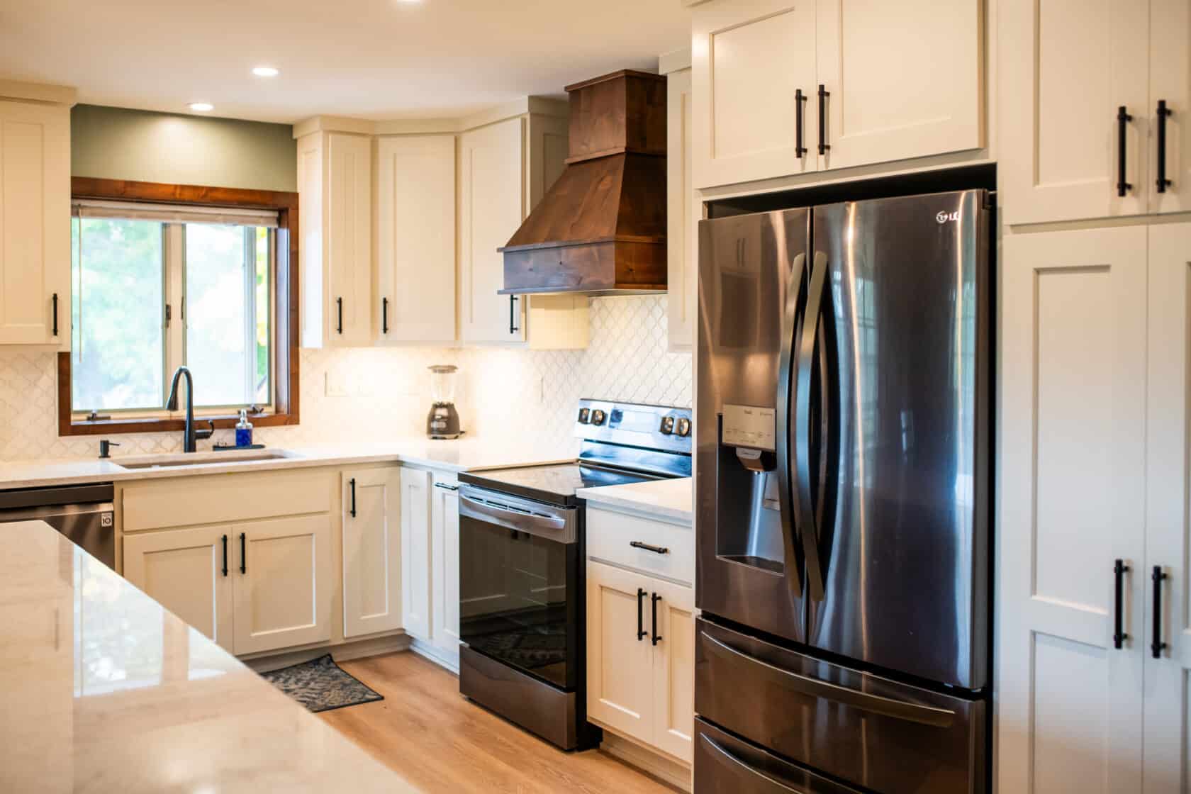 white painted kitchen cabinets with black stainless refrigerator and range and stained wood range hood